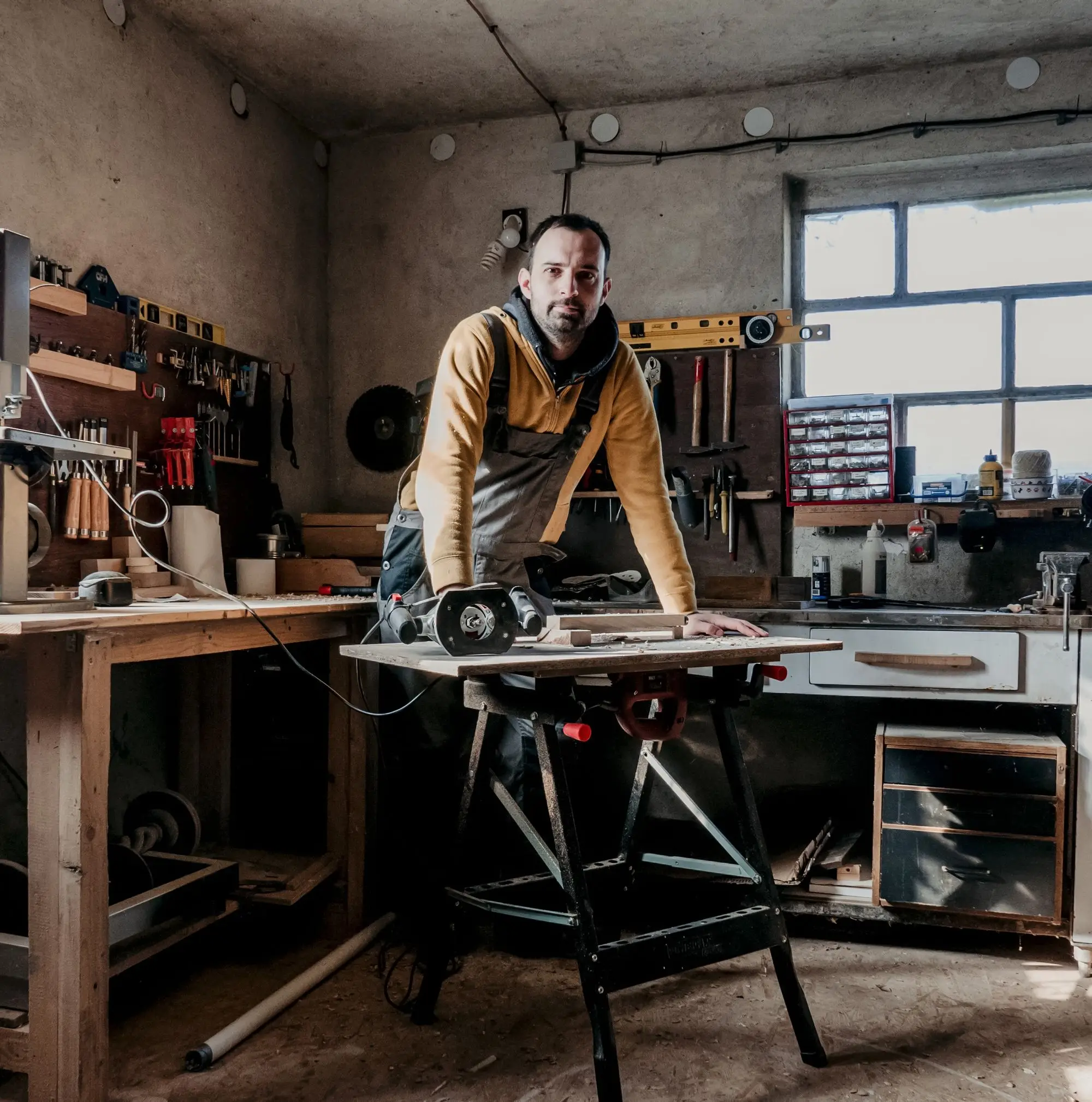 Joinery business owner leaning on a saw bench in his workshop, thinking about the years before selling
