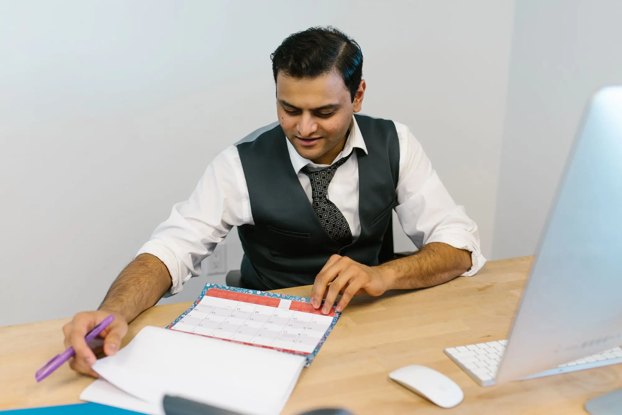 Business owner at his desk checking a planner while working out staff annual leave dates